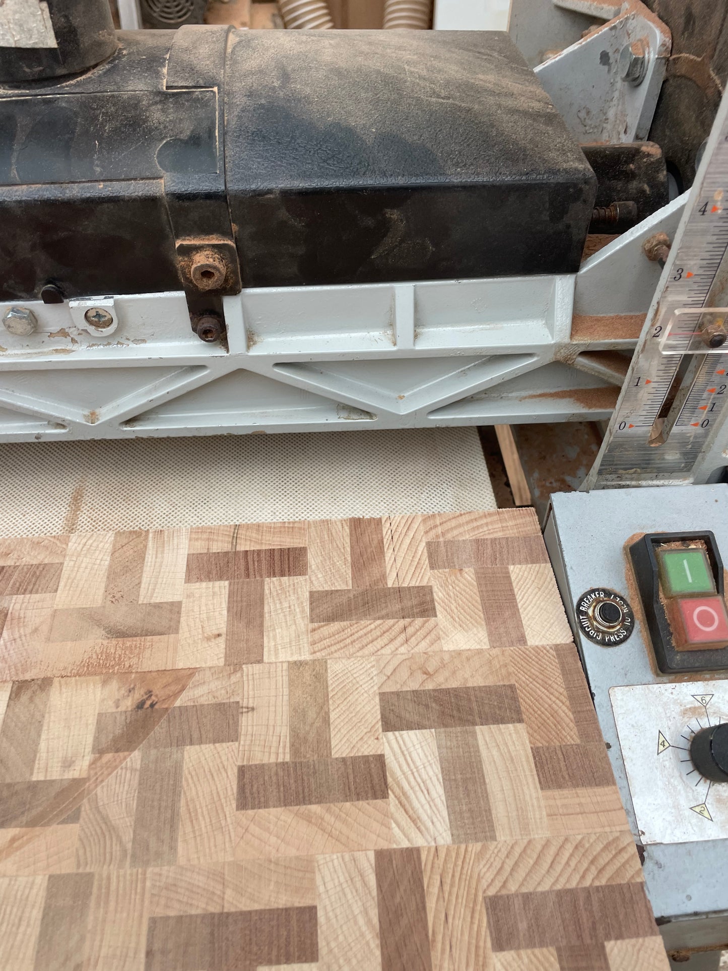Workshop video showing a handmade beech and sapele T-shape end grain chopping board passing through a sanding machine before final oiling and waxing.
