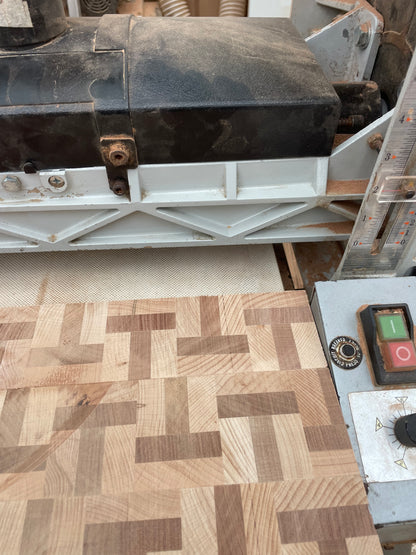 Workshop video showing a handmade beech and sapele T-shape end grain chopping board passing through a sanding machine before final oiling and waxing.