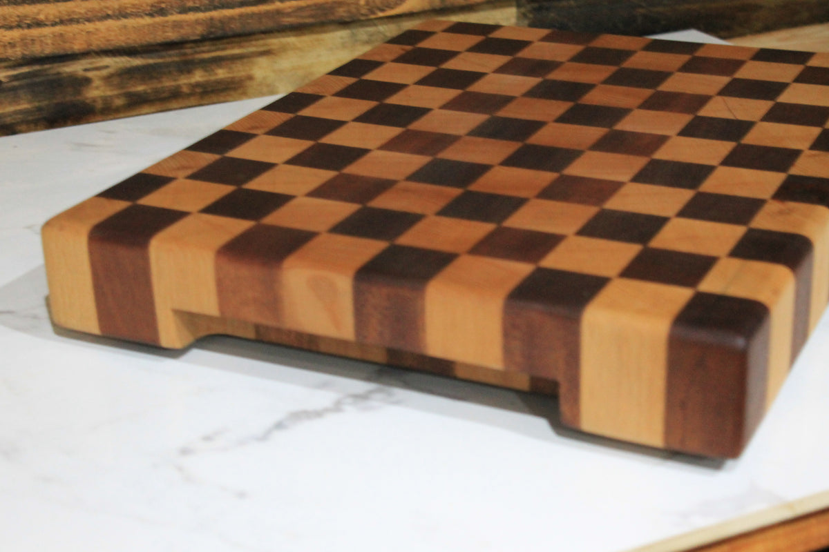 Angled close-up of handmade end grain chequered wooden chopping board showing its checkerboard hardwood pattern and thick solid wood edges. 