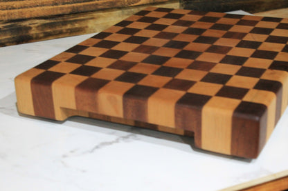 Angled close-up of handmade end grain chequered wooden chopping board showing its checkerboard hardwood pattern and thick solid wood edges. 