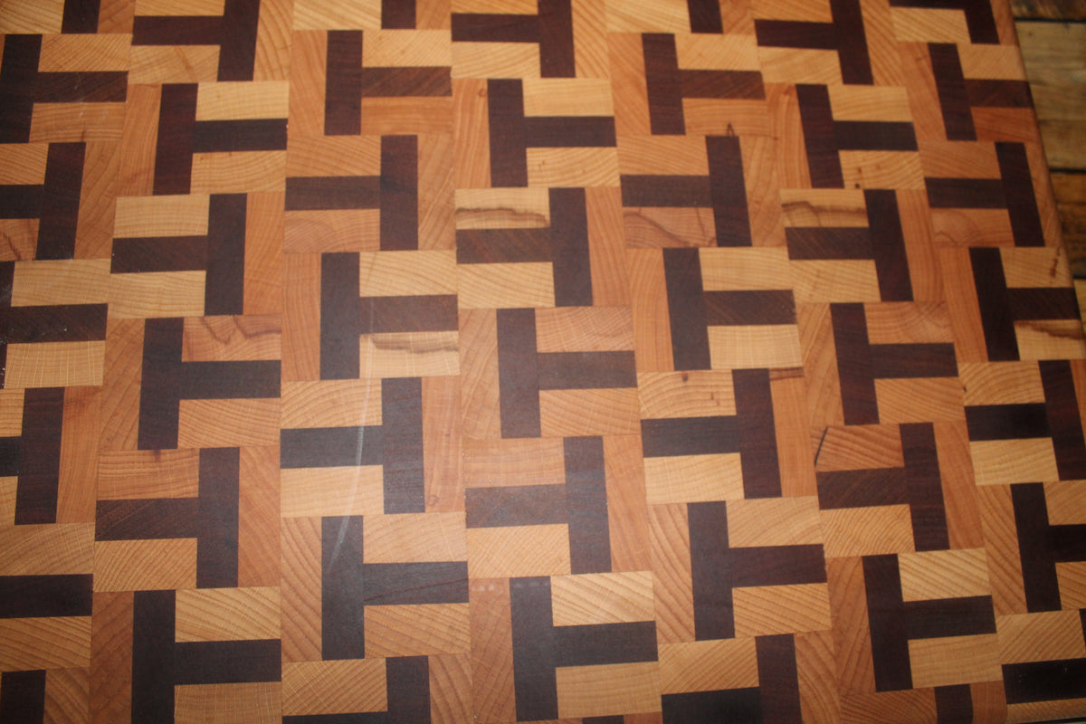 Close-up of a handmade end grain chopping board showing the geometric T-shape pattern in contrasting beech and sapele hardwoods. 