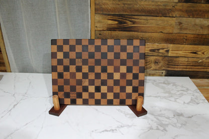 Handmade end grain chequered chopping board standing upright on its feet, displaying the contrasting hardwood checkerboard pattern.