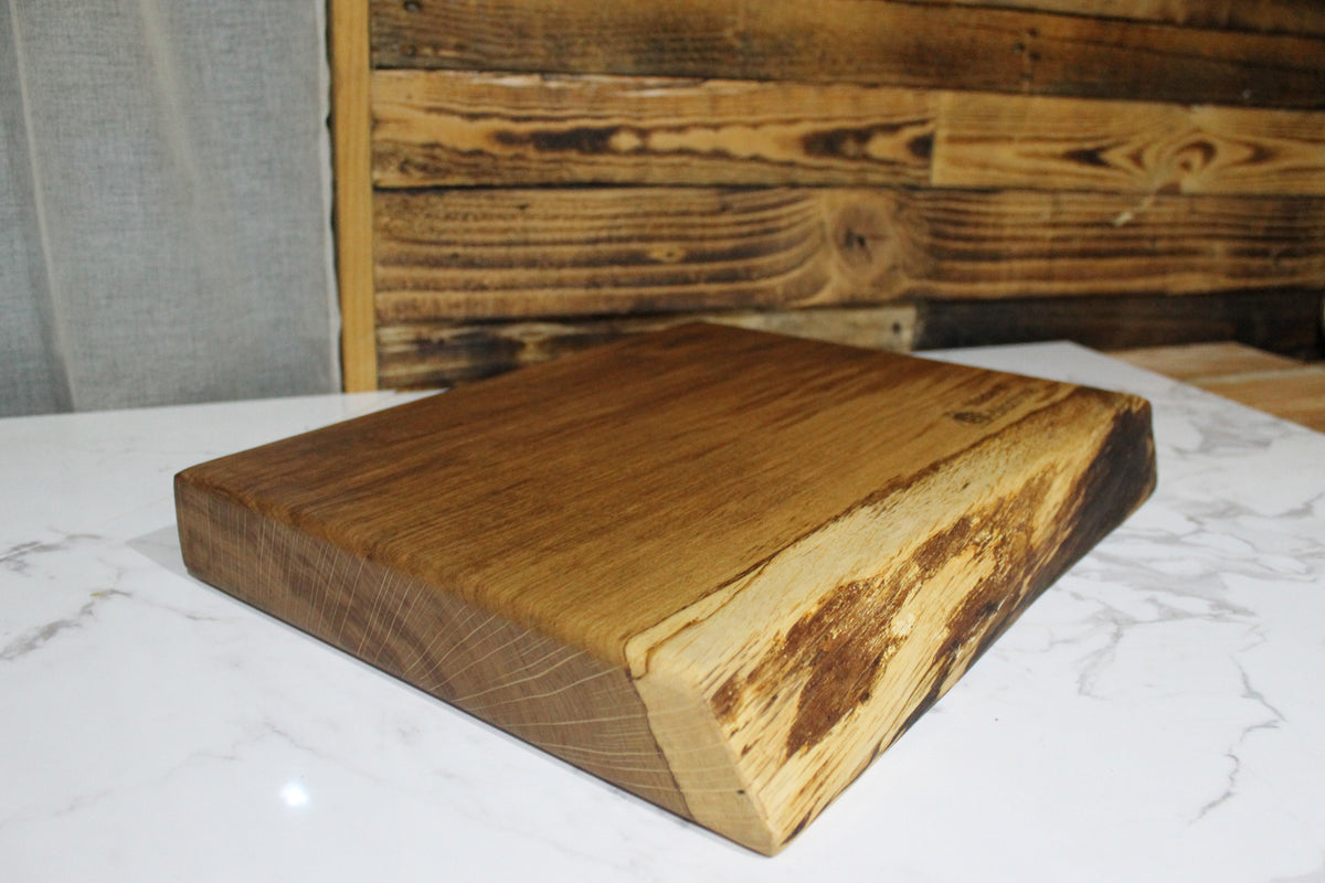Angled view of handmade solid oak live edge chopping board showing natural wood grain, thick hardwood construction and rustic edges.