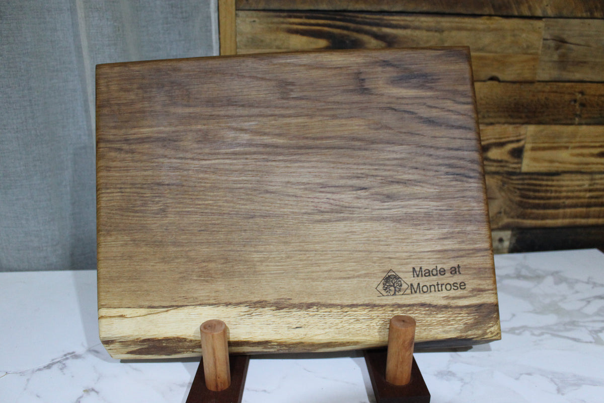 Handmade live edge oak  chopping board from the Montrose Estate in Lancashire, displayed upright to show its natural wood grain and rustic shape. 