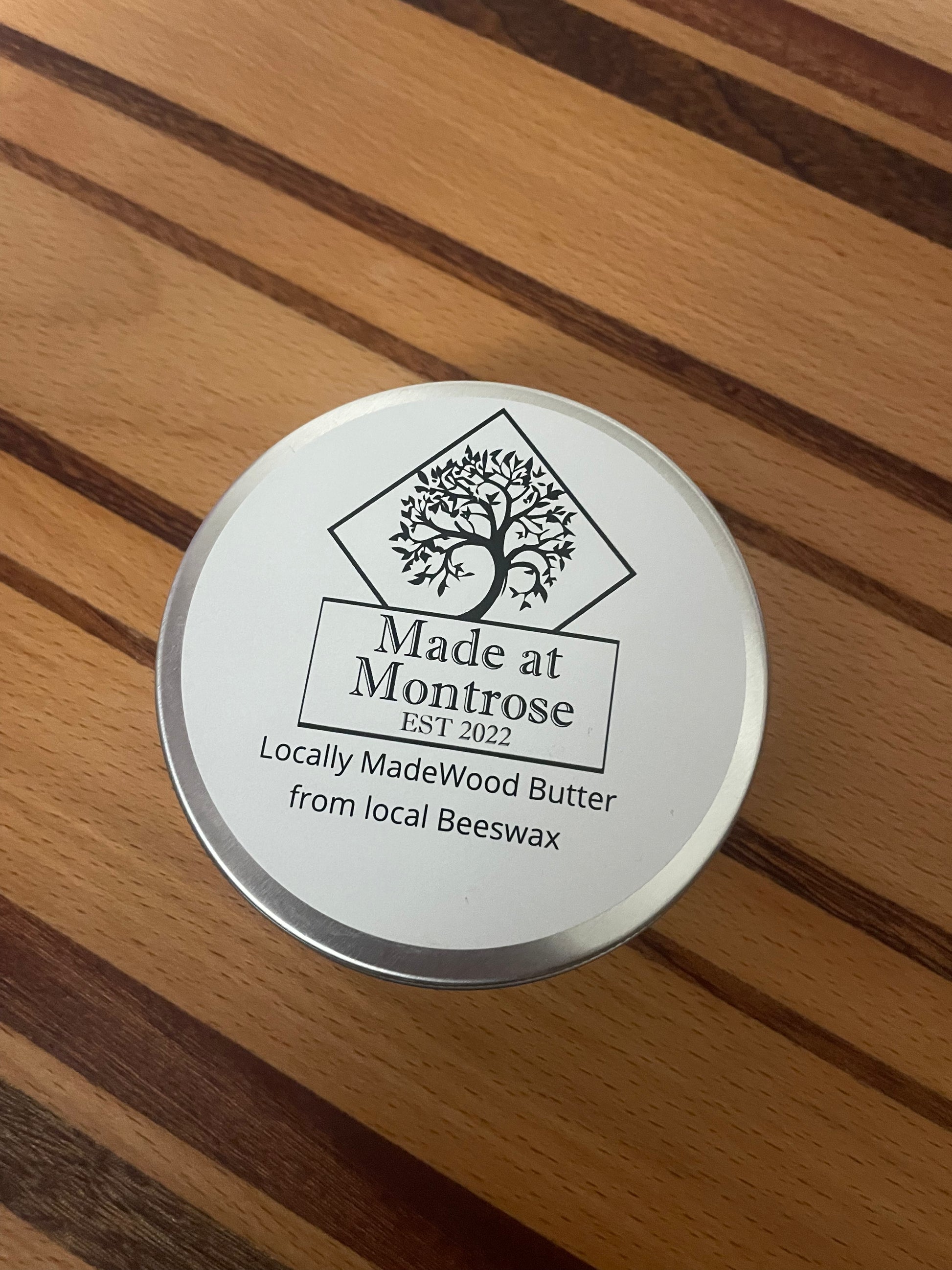 Made at Montrose Wood Butter 100ml tin with branded lid, displayed on a striped hardwood chopping board. 