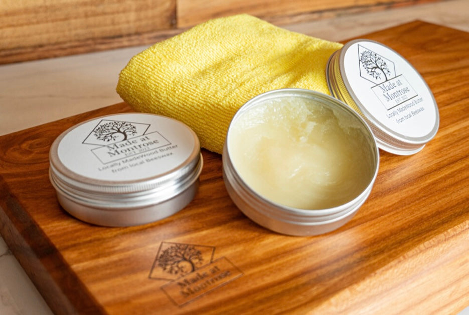 Made at Montrose Wood Butter with locally sourced beeswax, displayed in 100ml tins on a wooden chopping board.