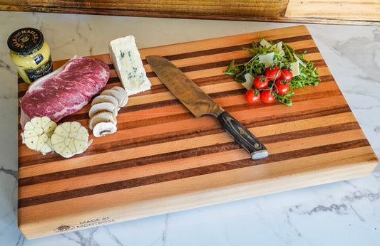 1 — "Handmade beech and sapele striped wooden chopping board displaying cheese, meats and fresh vegetables, crafted in Lancashire.