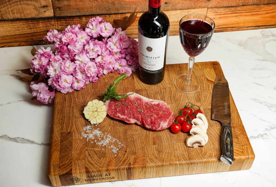 Overhead view of the Montrose Edition solid oak end grain chopping board, styled with food, flowers and red wine  